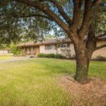 Front yard of a single-story brick house with a large tree and green lawn in College Station.