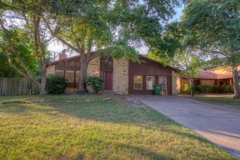 Front view of a residential house with a driveway and trees in the yard.