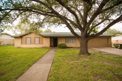 Front view of a single-story house with a large tree in the yard in Aggieland, Texas.