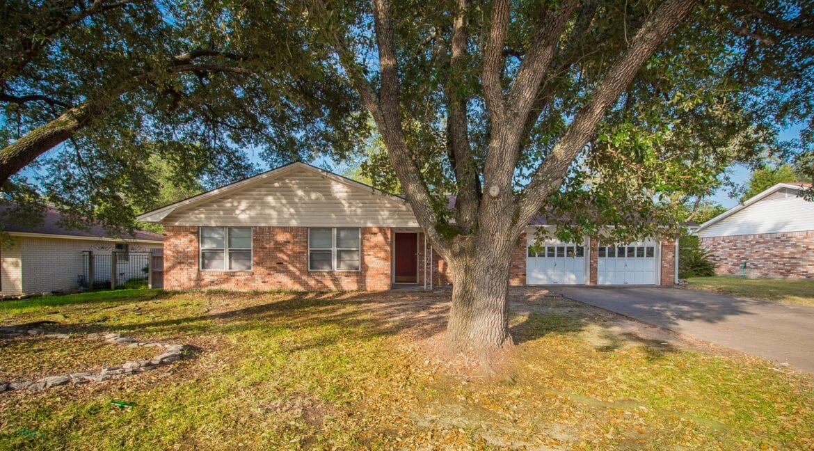 Front view of a brick and siding house with a large tree in the yard.