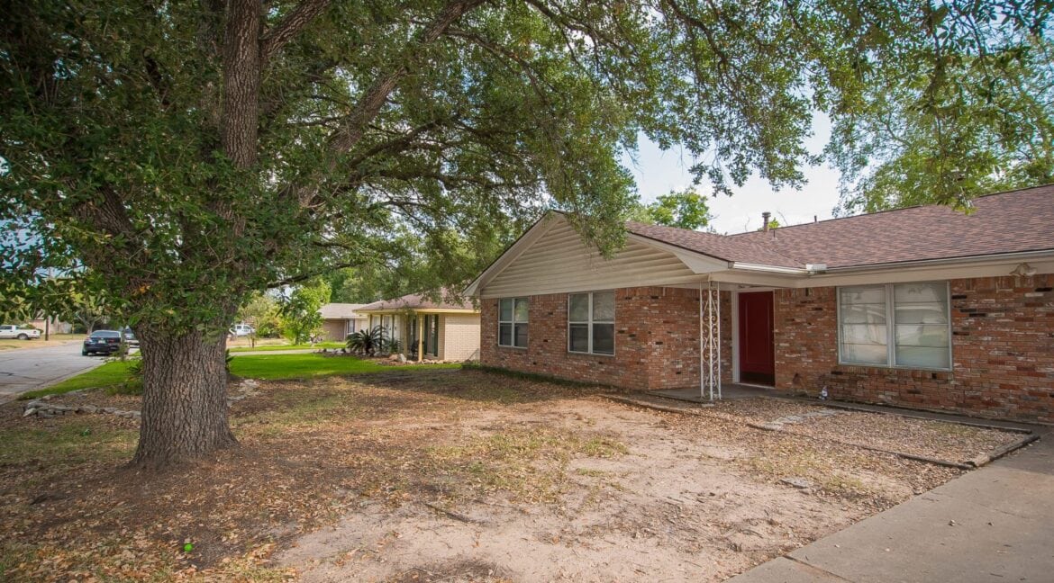 Exterior view of a brick house with a large tree in front, in a residential neighborhood.