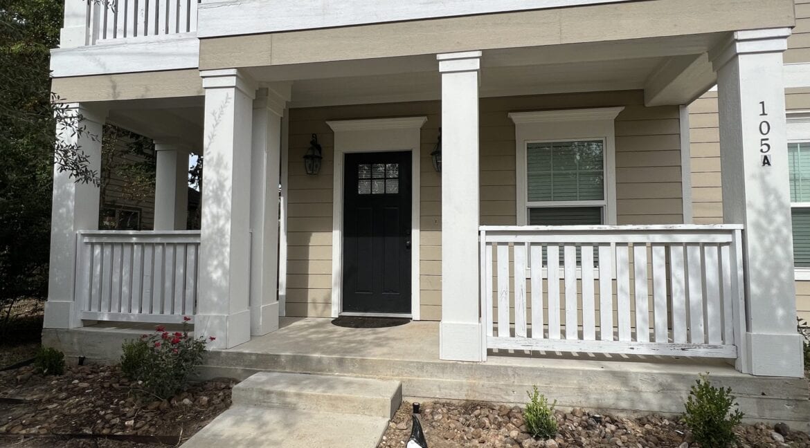 Front porch of a two-story house with beige siding and white railings in Aggieland.