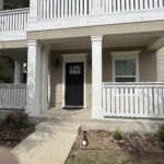 Front porch of a two-story house with beige siding and white railings in Aggieland.