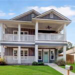 Two-story house with a large front porch and white railings in a suburban neighborhood.