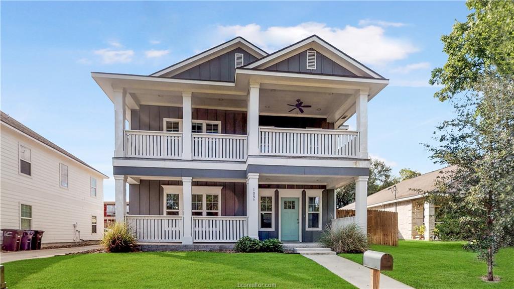 Two-story house with a large front porch and white railings in a suburban neighborhood.