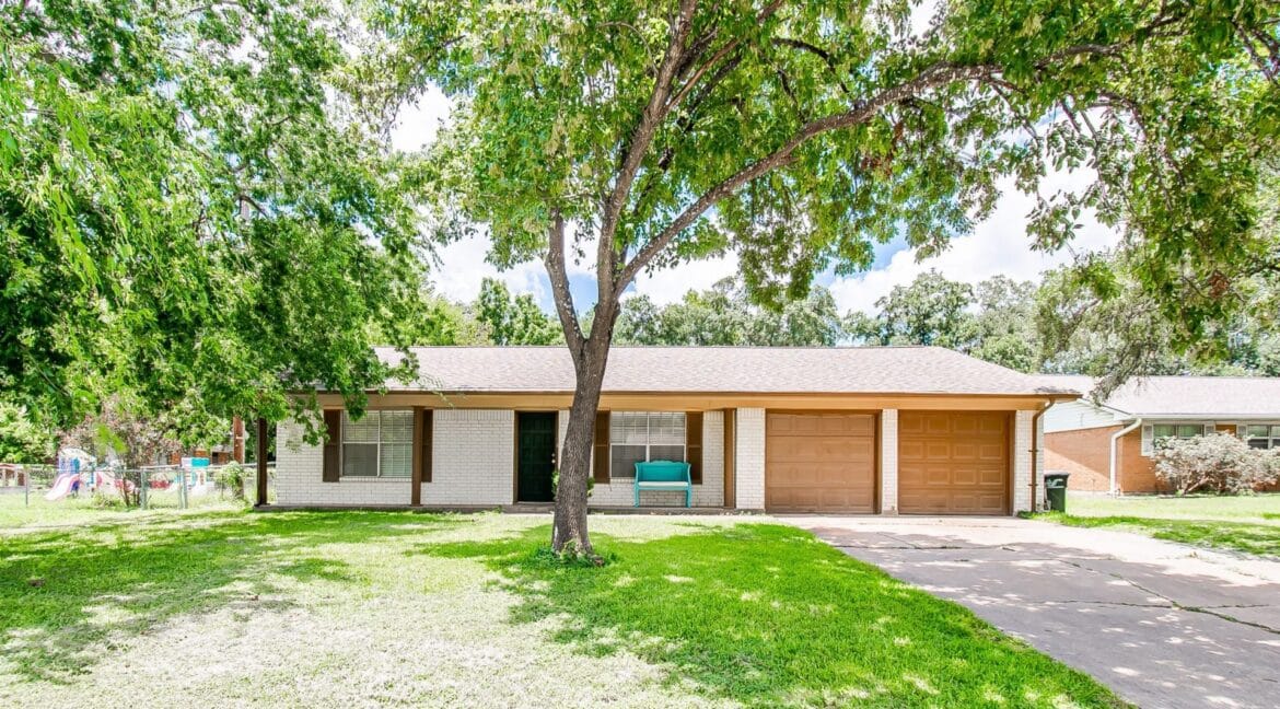 Single-story house with a brown garage door and a large front yard with a tree.