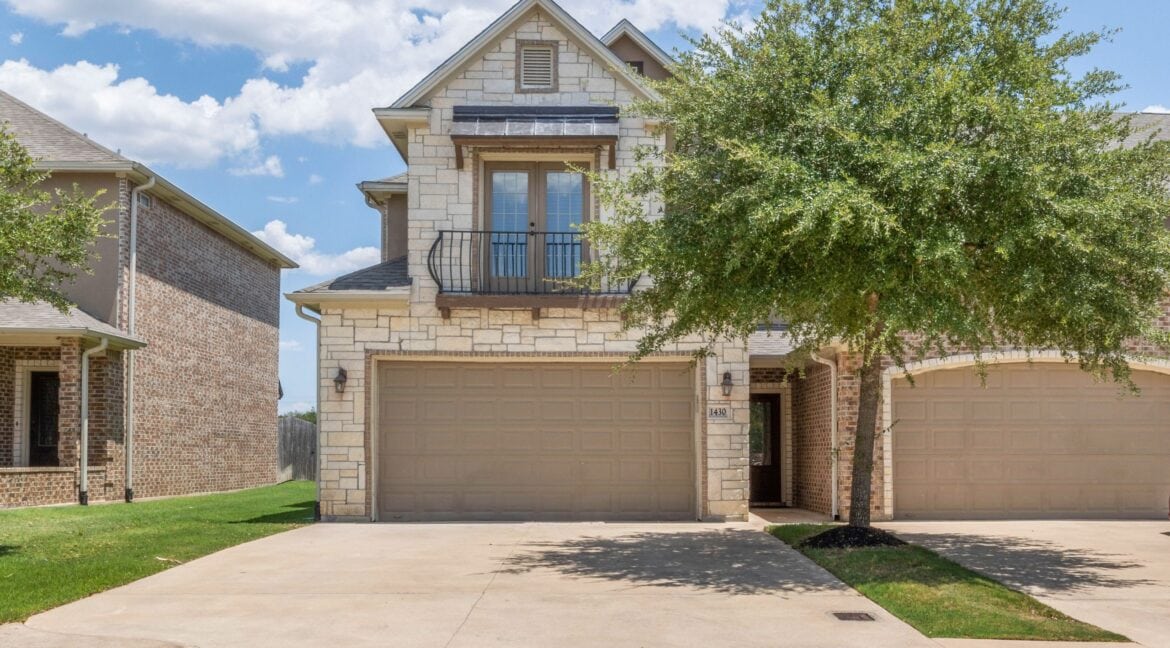 Modern two-story house with stone facade, balcony, and attached garage in Aggieland, Texas.