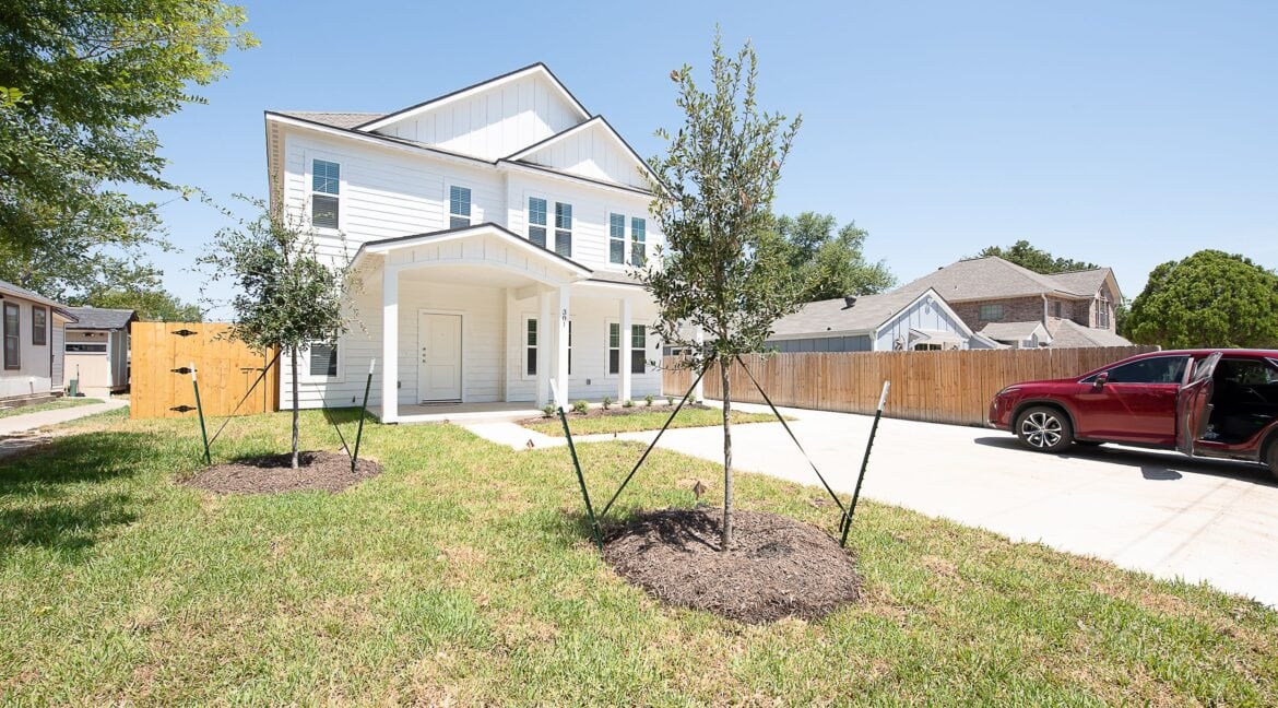 Newly built white house with a front yard and driveway in Aggieland, Texas.