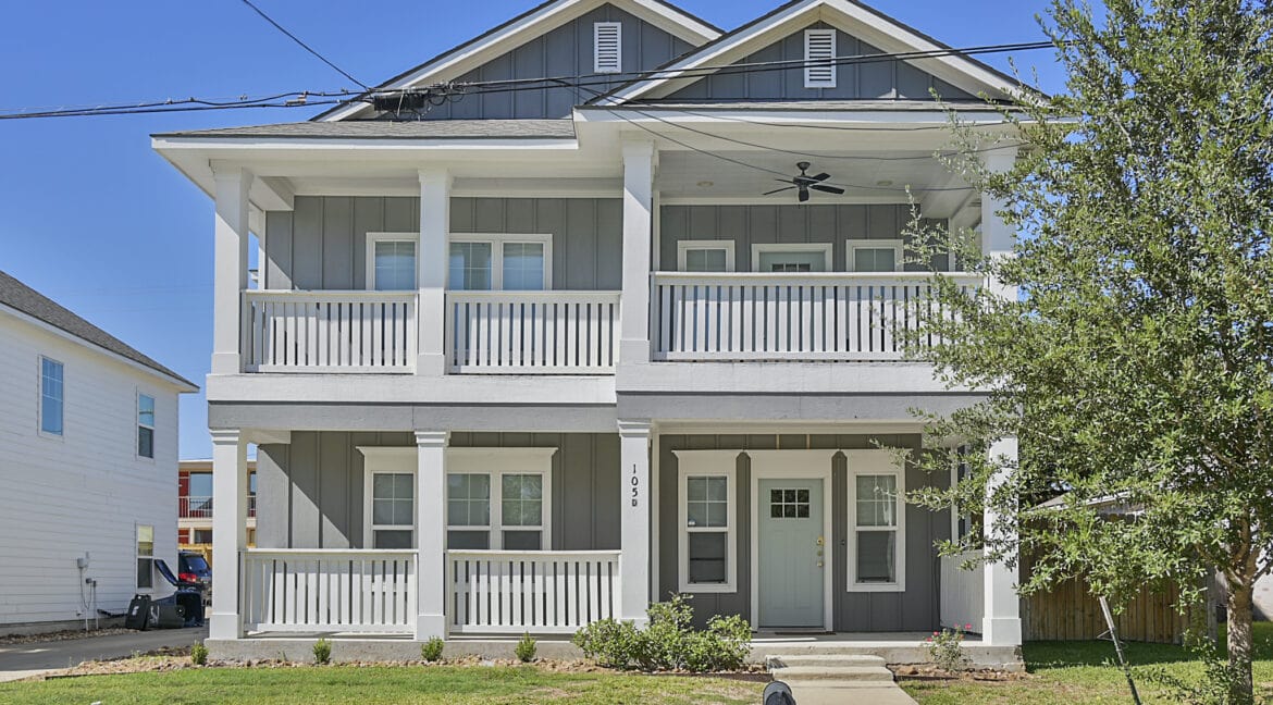 Front view of a two-story gray house with white porch railings and a front lawn.