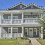 Front view of a two-story gray house with white porch railings and a front lawn.