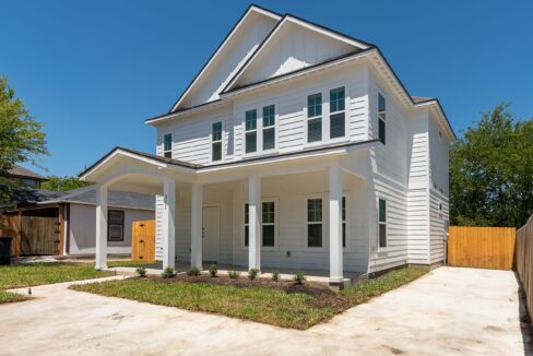 New white two-story house with front porch and multiple windows in a residential neighborhood.