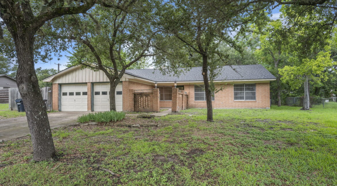 Brick house with attached garage and large front yard with trees in College Station, TX.