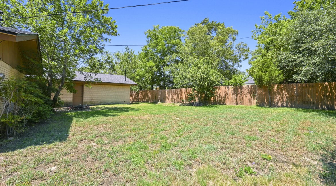Empty backyard with grass, trees, and a wooden fence in Aggieland, Texas.