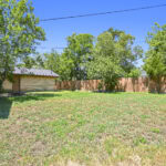 Empty backyard with grass, trees, and a wooden fence in Aggieland, Texas.
