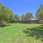 Spacious backyard with green grass, trees, and a wooden fence in a residential area.