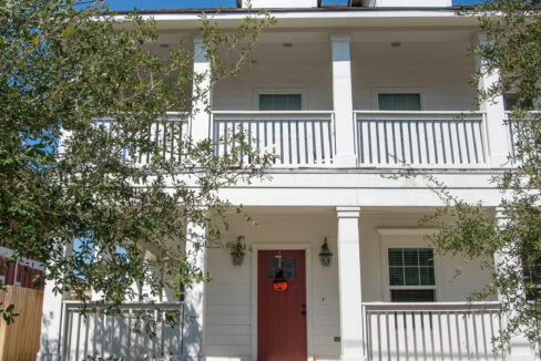 Three-story white house with a red front door and a small front yard under a clear blue sky.