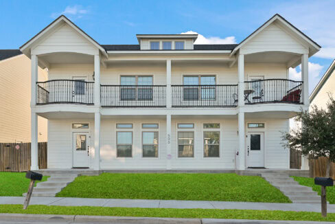 Front view of a two-story white residential building with balconies and steps leading to the entrance.