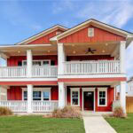 Red two-story house with white porch railings and a front yard in Aggieland, Texas.