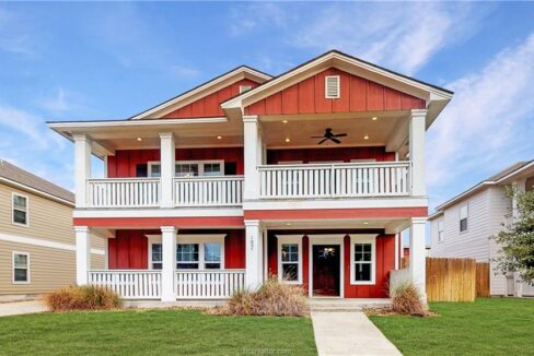 Red two-story house with white porch railings and a front yard in Aggieland, Texas.